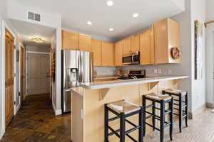 Kitchen with visible vents, light brown cabinetry, appliances with stainless steel finishes, a peninsula, and light countertops