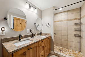 Full bathroom featuring double vanity, tiled shower, and a sink