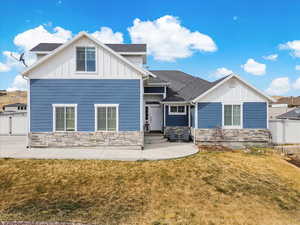 View of front facade featuring a front yard, fence, board and batten siding, and stone siding