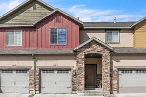 Townhome / multi-family property with stucco siding, a shingled roof, a garage, stone siding, and board and batten siding