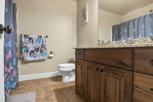 Full bathroom with vanity, a shower with shower curtain, baseboards, tile patterned floors, and toilet