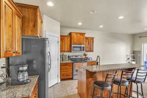 Kitchen with brown cabinets, a center island, recessed lighting, stainless steel appliances, and a breakfast bar area
