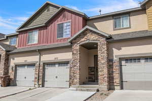 View of front of house featuring board and batten siding, stucco siding, a garage, stone siding, and driveway