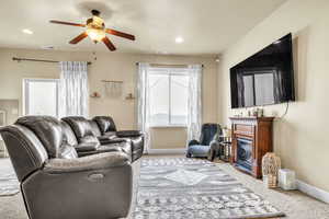 Carpeted living room with a ceiling fan, baseboards, visible vents, recessed lighting, and a glass covered fireplace