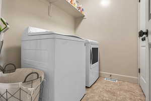 Clothes washing area with visible vents, baseboards, laundry area, and washer and clothes dryer