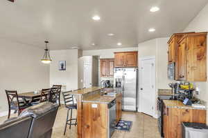 Kitchen with light stone countertops, a kitchen bar, appliances with stainless steel finishes, brown cabinetry, and a sink