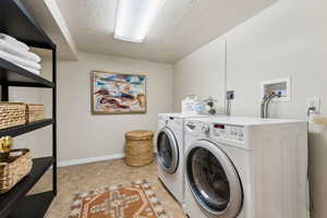 Clothes washing area featuring laundry area, washing machine and dryer, a textured ceiling, and baseboards