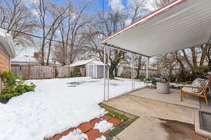 Yard layered in snow featuring a fenced backyard, a patio, a storage shed, and an outdoor structure