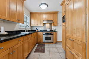 Kitchen with light tile patterned flooring, built in microwave, a sink, under cabinet range hood, and stainless steel oven