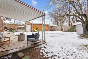 Snow covered deck with a garage, an outbuilding, and a fenced backyard