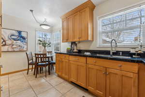 Kitchen with dark stone countertops, brown cabinetry, baseboards, light tile patterned flooring, and a sink