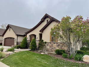 View of front of house featuring a front lawn, a garage, stone siding, concrete driveway, and stucco siding