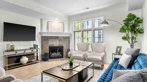 Living room with visible vents, wood finished floors, a tile fireplace, and ornamental molding