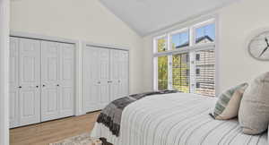 Bedroom with light wood-type flooring, lofted ceiling, and two closets