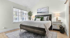 Bedroom with lofted ceiling, a barn door, wood finished floors, and baseboards