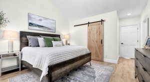 Bedroom featuring a barn door, lofted ceiling, baseboards, and light wood-style flooring