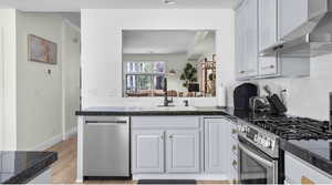 Kitchen featuring light wood finished floors, backsplash, wall chimney range hood, appliances with stainless steel finishes, and a sink