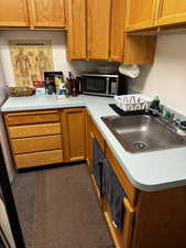 Kitchen featuring stainless steel microwave, light countertops, brown cabinets, and a sink