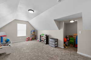 Recreation room with a textured ceiling, baseboards, carpet flooring, and lofted ceiling