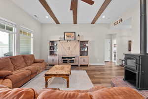 Living room with visible vents, beamed ceiling, wood finished floors, and a wood stove