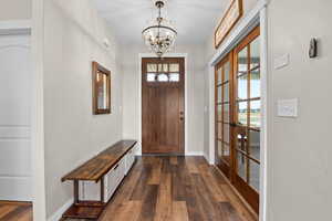 Entryway featuring dark wood-style floors, plenty of natural light, baseboards, and an inviting chandelier