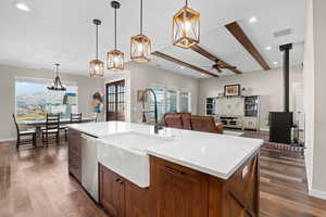 Kitchen featuring beam ceiling, dark wood-style flooring, light countertops, stainless steel dishwasher, and a sink