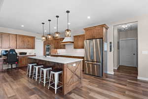 Kitchen featuring appliances with stainless steel finishes, a kitchen island with sink, dark wood-style flooring, and light countertops