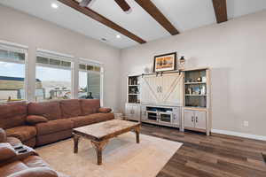 Living area featuring dark wood-style floors, beam ceiling, a barn door, a ceiling fan, and baseboards