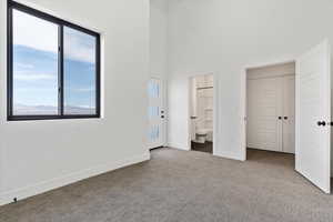Unfurnished bedroom with ensuite bath, baseboards, a high ceiling, and carpet