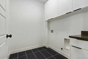 Washroom with hookup for a washing machine, dark tile patterned flooring, cabinet space, and baseboards