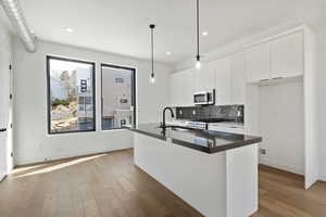Kitchen with a sink, dark countertops, light wood-style floors, appliances with stainless steel finishes, and decorative backsplash