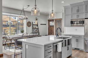Kitchen featuring gray cabinetry, light countertops, wood finished floors, stainless steel appliances, and a kitchen island with sink