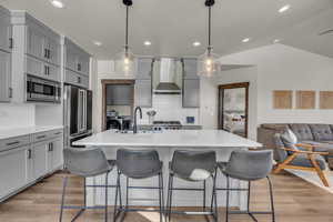 Kitchen with gray cabinets, a sink, light wood-style floors, appliances with stainless steel finishes, and wall chimney range hood