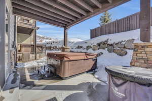 Snow covered patio featuring cooling unit, a mountain view, a hot tub, and fence