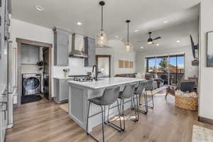 Kitchen featuring gray cabinetry, washer and clothes dryer, open floor plan, light countertops, and wall chimney exhaust hood