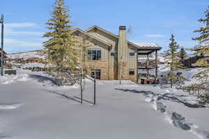 Snow covered rear of property featuring fence, board and batten siding, stone siding, and a chimney
