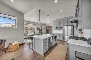 Kitchen featuring a kitchen breakfast bar, ventilation hood, appliances with stainless steel finishes, and gray cabinetry
