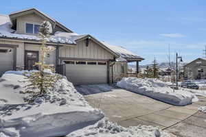 View of front of house with stone siding, board and batten siding, an attached garage, and driveway
