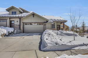 View of front of property with stone siding, board and batten siding, an attached garage, and driveway