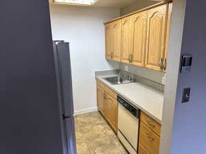 Kitchen featuring a sink, freestanding refrigerator, white dishwasher, light countertops, and baseboards