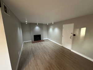 Unfurnished living room featuring a fireplace with raised hearth and wood finished floors