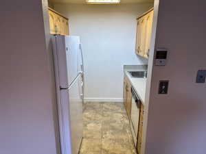 Kitchen featuring a sink, stainless steel dishwasher, freestanding refrigerator, light countertops, and baseboards