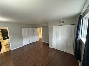 Unfurnished bedroom featuring visible vents, two closets, baseboards, and wood finished floors