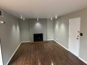 Unfurnished living room with dark wood finished floors, visible vents, a fireplace with raised hearth, and baseboards