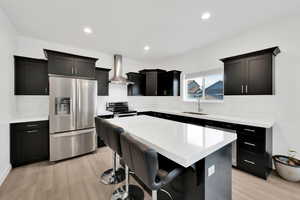 Kitchen with a sink, a center island, light wood-style floors, appliances with stainless steel finishes, and wall chimney exhaust hood