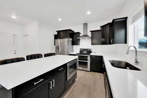 Kitchen featuring dark cabinets, appliances with stainless steel finishes, wall chimney range hood, and a sink