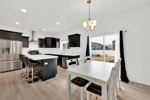 Kitchen with a center island, a kitchen bar, appliances with stainless steel finishes, light wood-style floors, and wall chimney exhaust hood