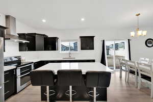 Kitchen with a breakfast bar, a sink, dark cabinetry, stainless steel appliances, and wall chimney exhaust hood