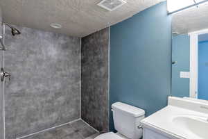 Bathroom with toilet, tiled shower, visible vents, and a textured ceiling