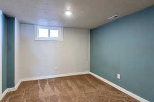 Basement featuring visible vents, baseboards, a textured ceiling, and carpet flooring